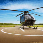 Čierny vrtuľník stojaci na pristávacej ploche s modrou oblohou v pozadí, pripravený na vzrušujúci letecký zážitok.