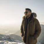 Turista stojí v zasneženej krajine oblečený v zimnej bunde a pevných topánkach.