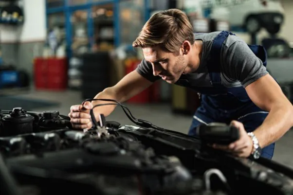 Automechanik pripájajúci štartovacie káble k motoru auta