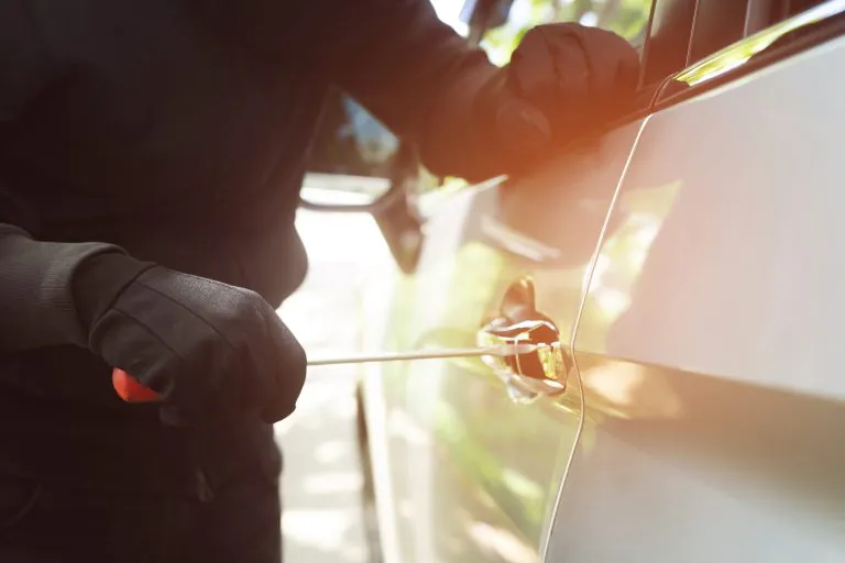 Poškodené auto s preliačinou a škrabancami po vandalizme na parkovisku.